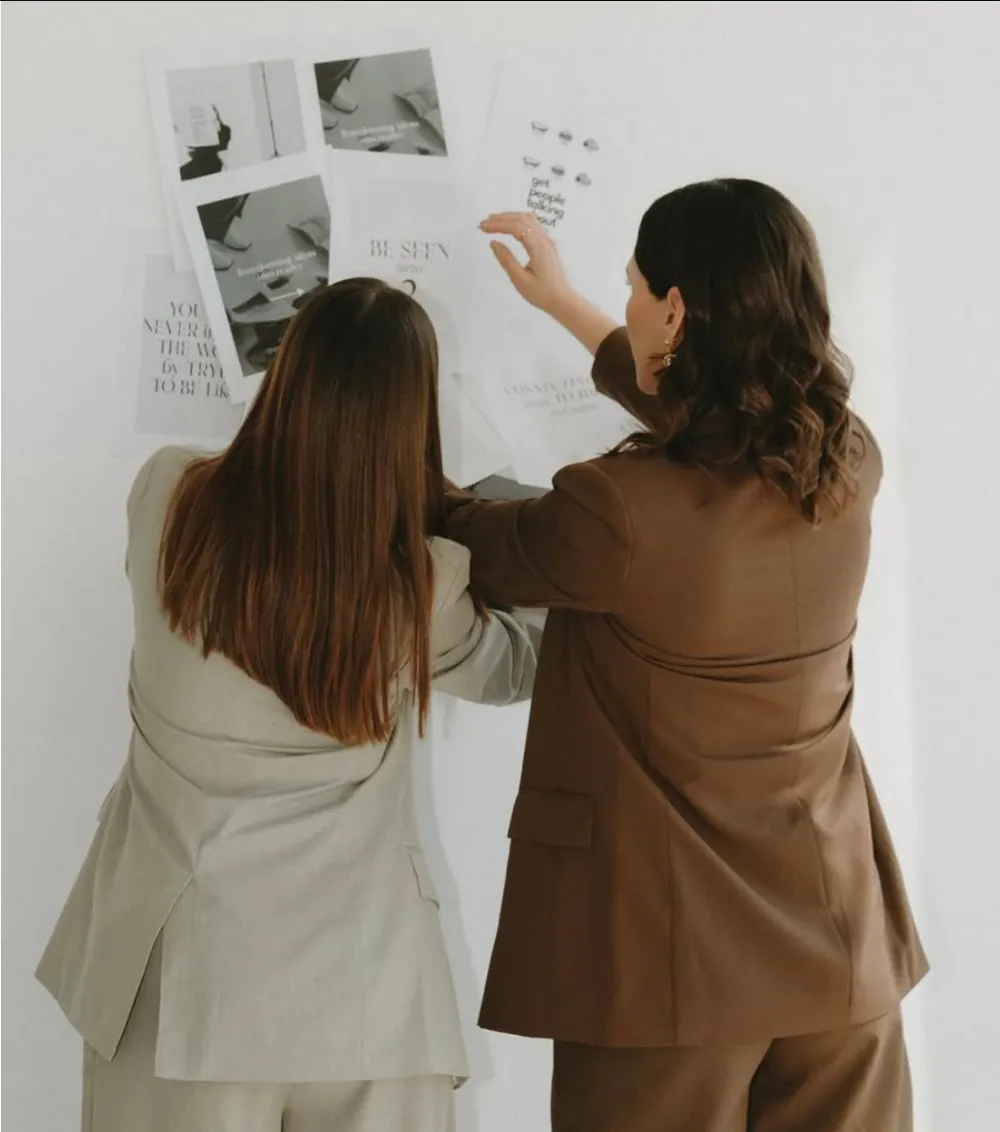 Las fundadoras de Be Seen acomodan un moodboard en la pared del estudio