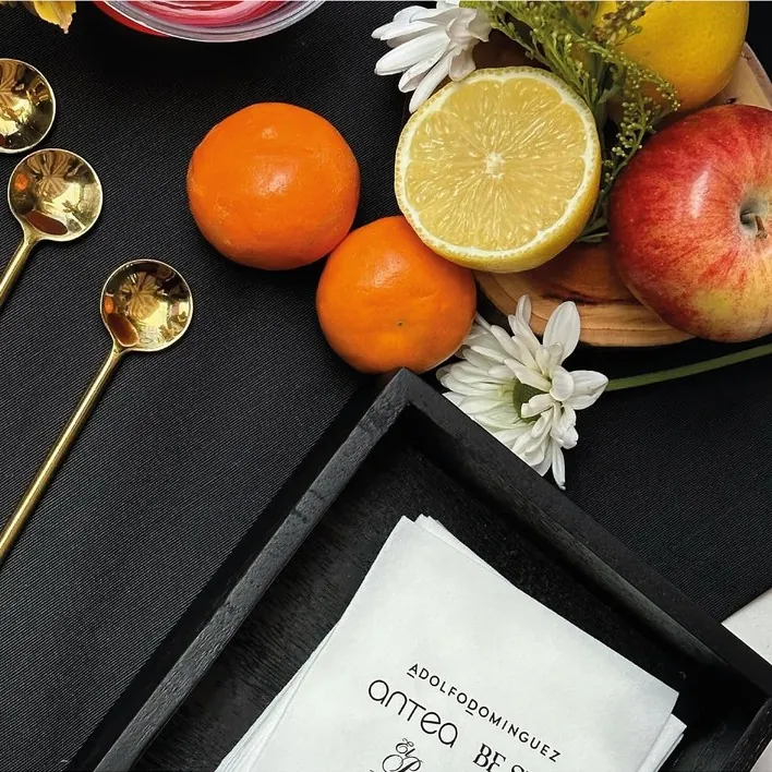 Mesa de bienvenida con fruta, cucharas doradas y tarjeta impresa